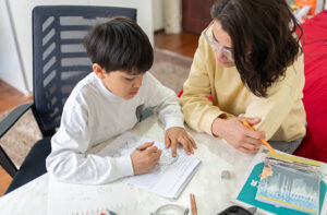 Female Teacher Helping Child Doing Homework During Private Lesson At Home